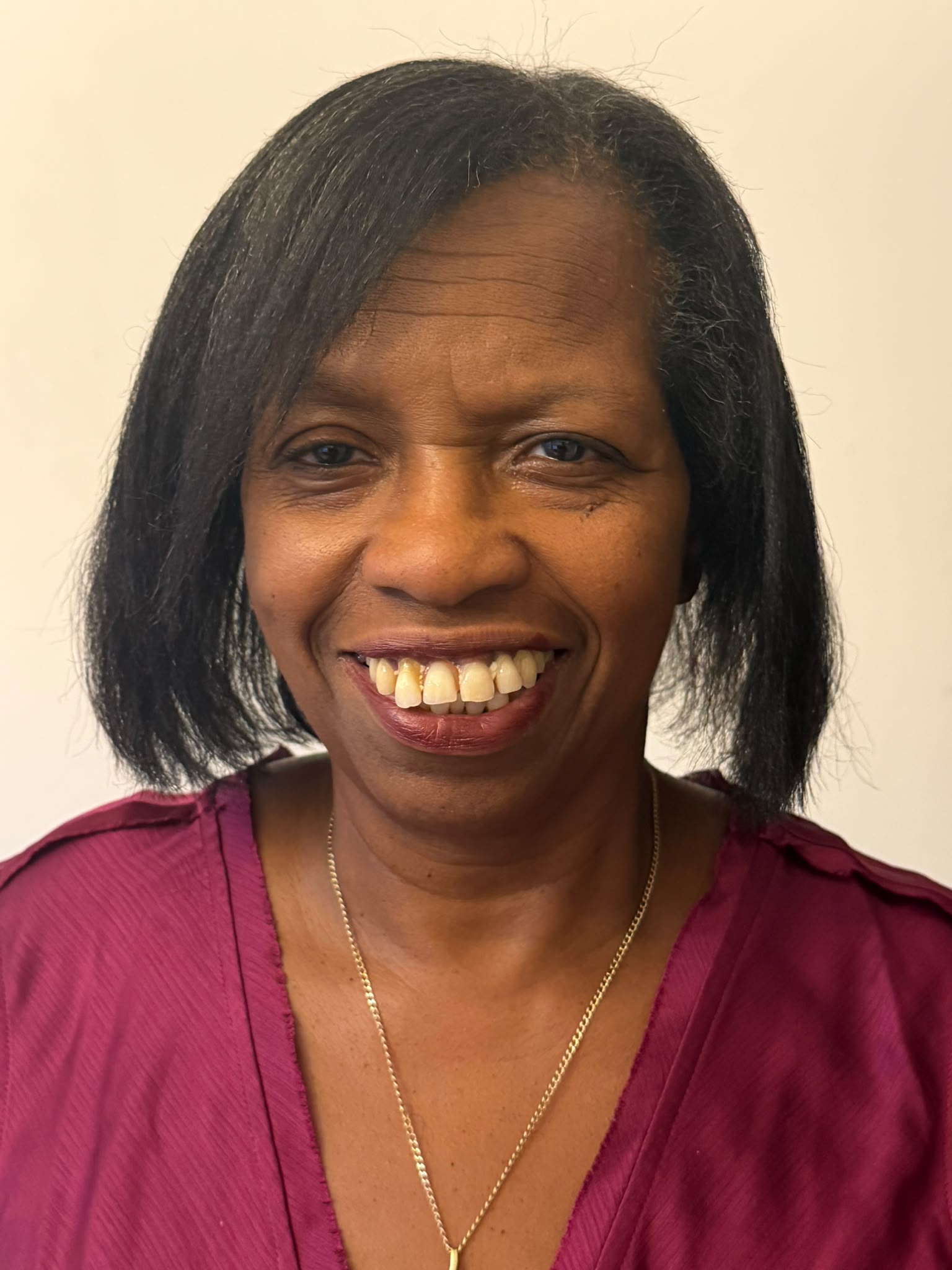 A picture of Sharon. She is wearing a white dress and has short straight black hair. She is wearing a necklace with a cross pendant.